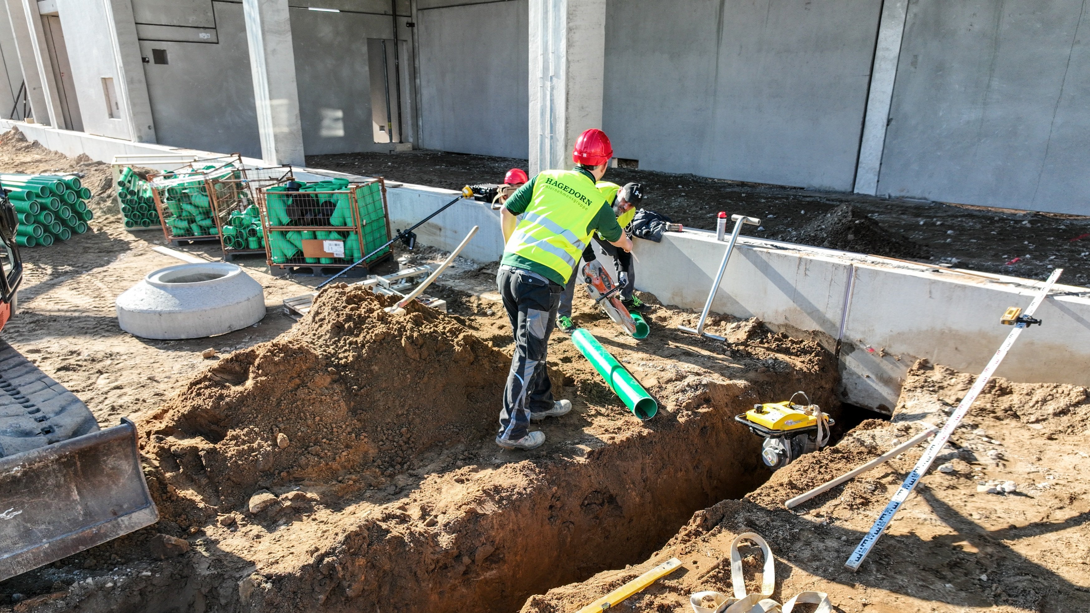 Bauarbeiter installiert grüne Rohre in Grube.